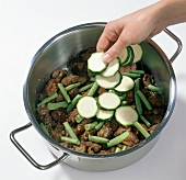 Beans and zucchini slices being added to fried meat in pot, step 3