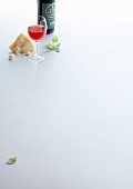 Bottle and glass with red wine and piece of cheese on white background, copy space