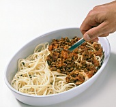 Layer of meat sauce being spread on spaghetti and eggplant slices in baking dish