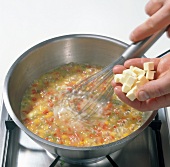 Butter cubes being added to peppers and stirred in pot