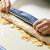 Dough sheet with toasted breadcrumbs and nuts being rolled with cloth