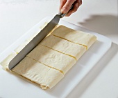 Folded dough being cut into rectangles on cutting board