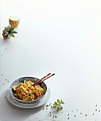 Pasta with pepper chicken in bowl with halved pineapple on white surface, copy space