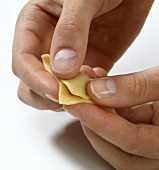Edges of stuffed pasta sheet being pressed for preparing tortellini, step 1