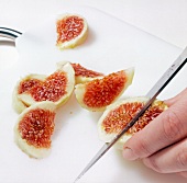 Peeled fig being cut into thin slices with knife