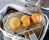 Three brown fried buns removed from frying basket to drain, overhead view