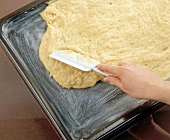 Dough being spread by spatula on butter greased baking tray