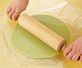 Green dough rolled under plastic with rolling pin