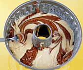Gugelhupf with light and dark batter being stirred in baking bowl on yellow background