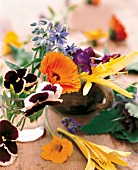 verschiedene essbare frische Blüten im Glas, Tasse auf einem Tisch