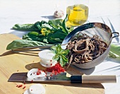 Wheat noodles in sieve with fresh vegetables and chopper on wooden board