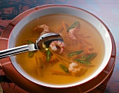 Clear tomato soup with vegetables and shrimp in bowl