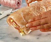 Close-up of woman's hands wrapping roll with string loop to roast