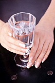 Glas Wasser in den Händen, french manicure, close-up.