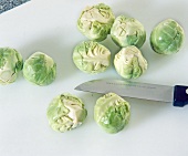 Brussels sprouts with dead leaves cutted on white chopping board with knife