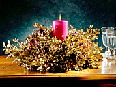 Lit pink candle in advent floral arrangement decorated with pink balls and golden sparkles