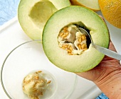 Scraping seeds from half a melon in glass bowl