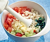 Bread cubes, tomatoes, cucumbers and other vegetables in a bowl with hand blender