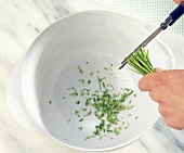 Chives being cut with kitchen shears over a bowl