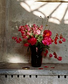 Ein Strauß roter und rosaner Blumen in einer dunkleroten Vase