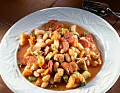 Close-up of bean stew with garlic sausage, carrots, pork and leek on plate
