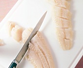 Close-up of fillet cut in pieces with knife while preparing cod with curry