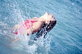 Frau im roten Badeanzug, Kopf im Nak -ken spritzt mit den Armen im Wasser