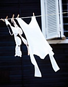 Close-up of two white bras and a cotton shirt hanging on clothesline drying in the wind