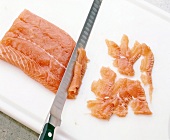 Salmon fillet being sliced with salmon knife on chopping board