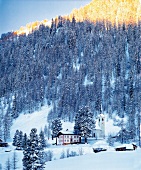 View of chapel on the hillside with pine trees and snow