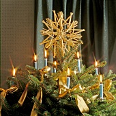 Fir tree top decorated with lit candles and straw star