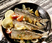 Close-up of herrings with onions, tomatoes and slices of lemon in pan