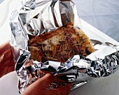 Close-up of roasted pork being wrapped in aluminium foil