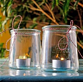 Lit tea light candles in glass jam jars tied