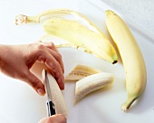 Banana being peeled and sliced on chopping board
