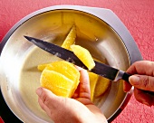 Slicing orange fruit in bowl