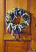Wreath made of green branches with blue and white ribbons on wooden door