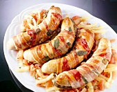 Close-up of stuffed bacon wrapped sausages with tomato and onion on plate
