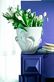 Vase with white tulips against purple wall