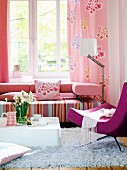 Living room with couch in shades of pink below window; designer armchair and coffee table