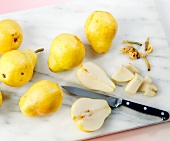 Whole and two halves of pear with knife on chopping board