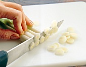 Close-up of spring onions being sliced into narrow rings on chopping board