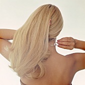 Frau mit langen blonden Haaren tupft sich Parfum auf den Nacken