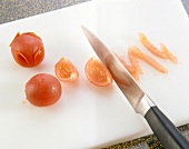 Cherry tomatoes being chopped into thin strips on chopping board