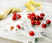 Cherries with cherry pitter, grapes and sliced banana on chopping board