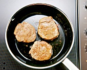 Close-up of three pieces of meat in pan