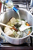 White wine being poured in pan with fish remains, vegetables, herbs and spices, step 1