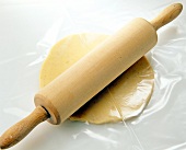 Close-up of rolling pin on dough wrapped in plastic