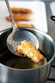 Fried fish stick in skimmer being removed from cooking oil