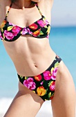 Sexy woman wearing colourful floral pattern bikini on beach, mid section